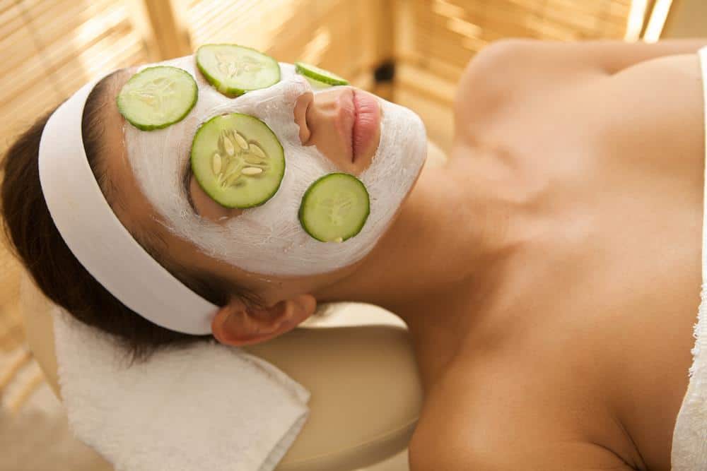 Young woman lying down on massage table with cucumbers on eyes and face